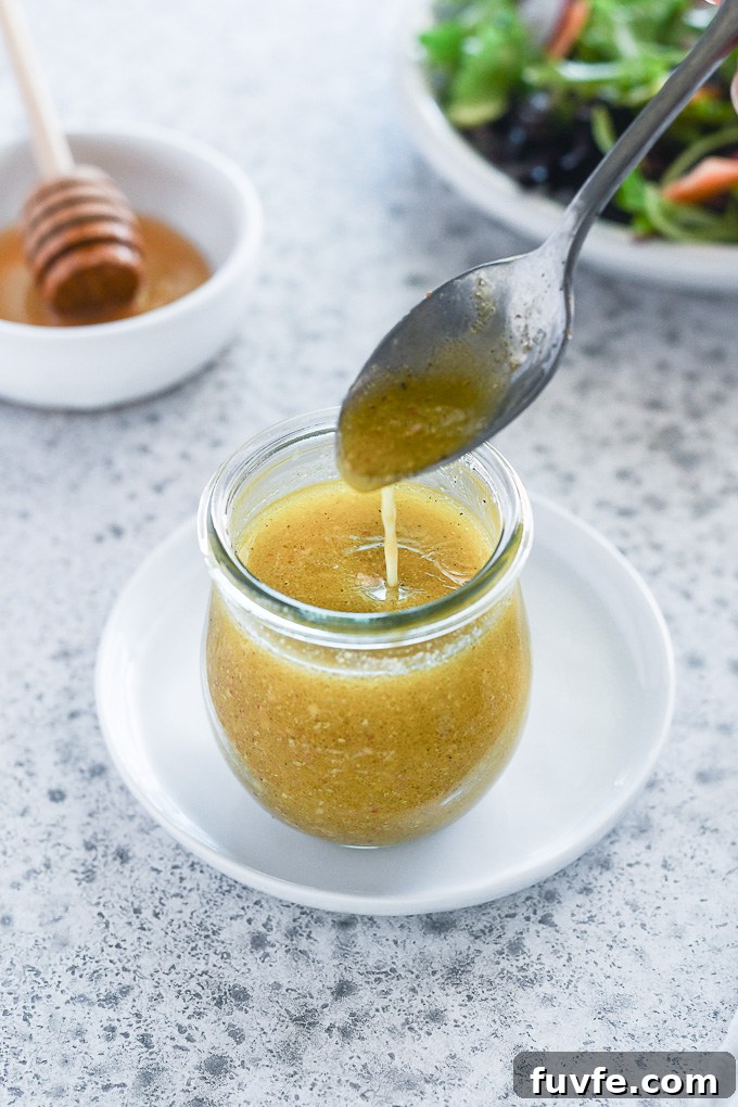 spoon drizzling honey mustard dressing into a jar