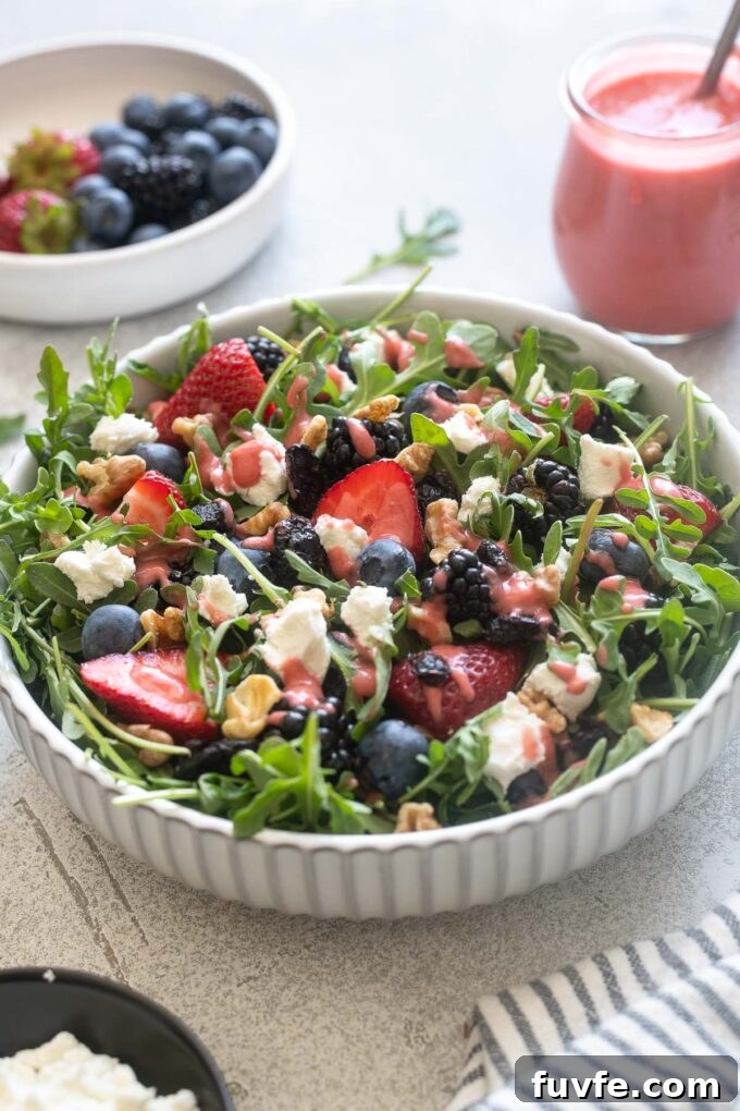 Fresh Berry and Arugula Salad Recipe with Goat Cheese 6 Arugula and goat cheese salad in a white bowl with dressing.