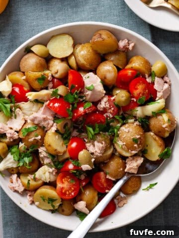 A big bowl of tuna potato salad on a napkin with two small plates of the salad off to the side.