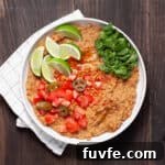 A bowl of vegan refried beans topped with cilantro, tomatoes, limes and pickled jalapenos.