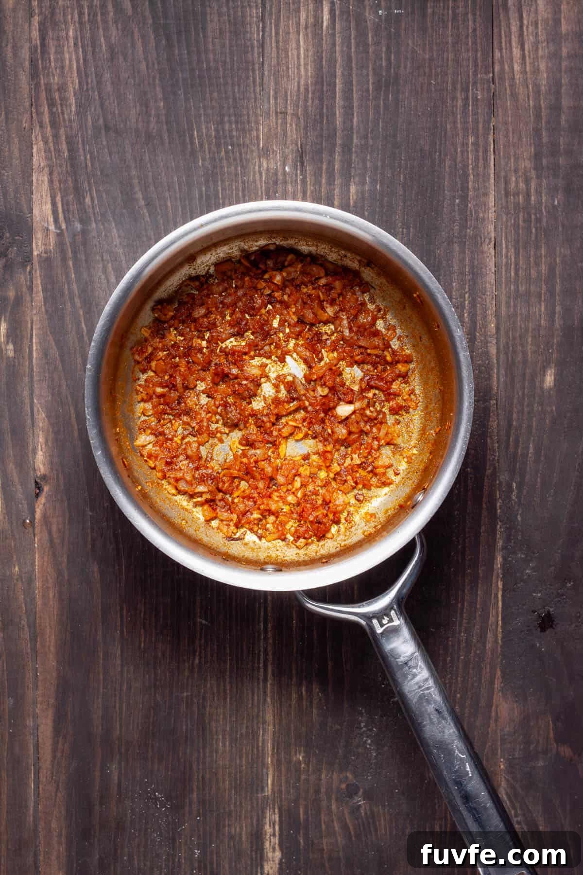 Minced onion and garlic cooking in a saucepan with cumin and paprika.