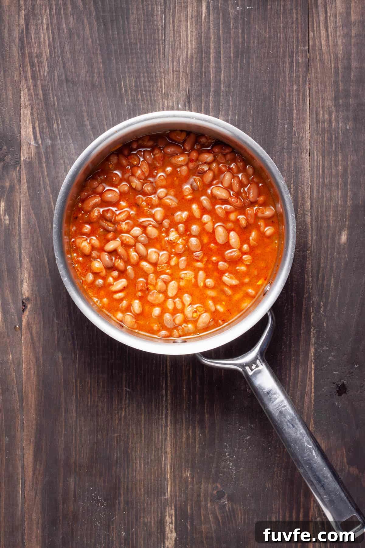 Pinto beans in a saucepan cooking with vegetable broth and aromatics.