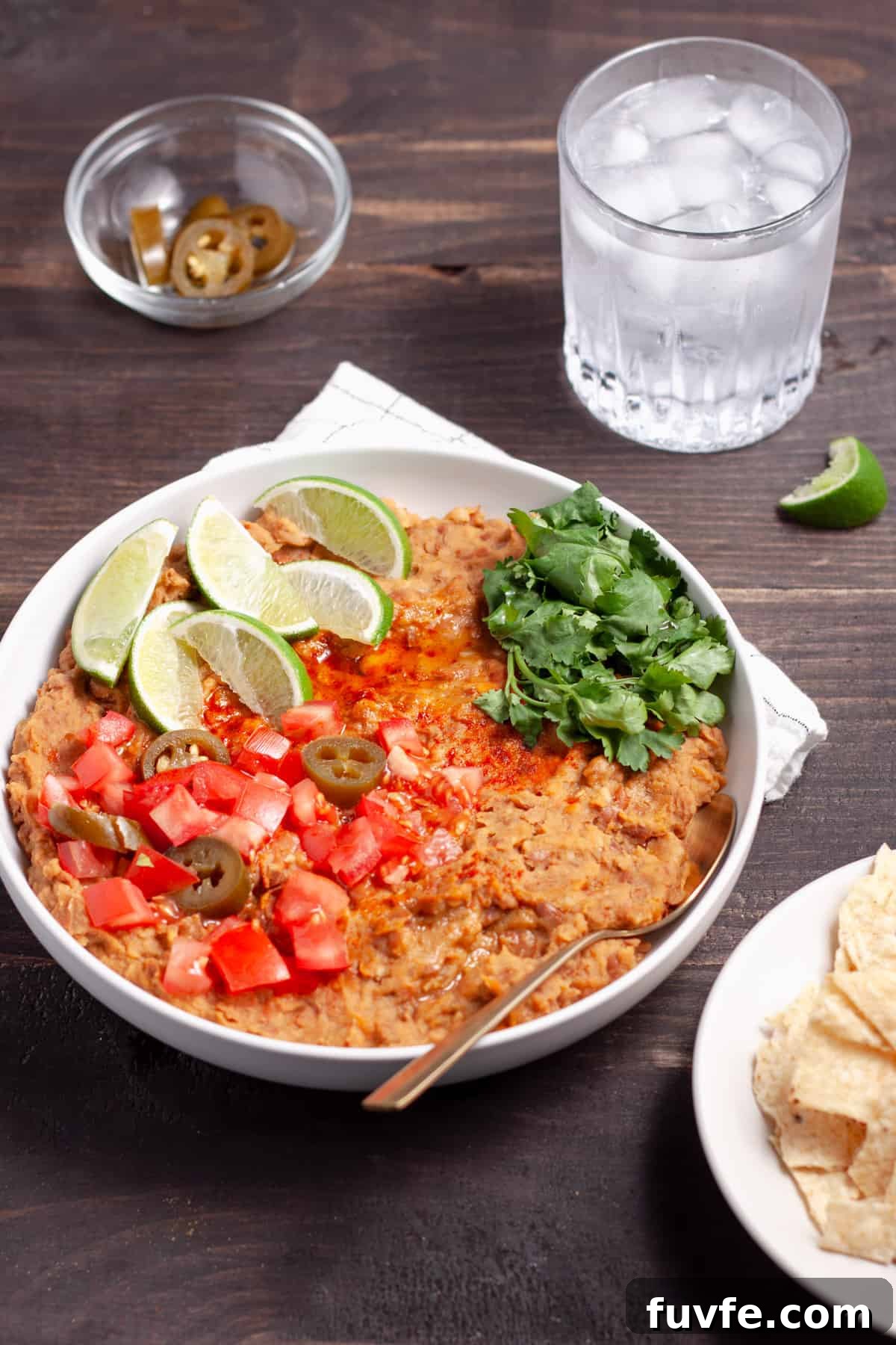 A bowl of vegan refried beans topped with cilantro, tomatoes, limes and pickled jalapenos.