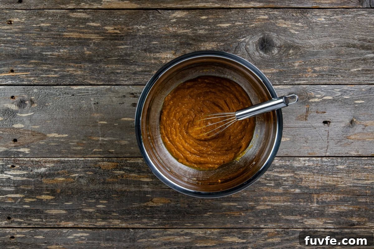 Pumpkin puree, oil, and milk in a mixing bowl with a whisk.