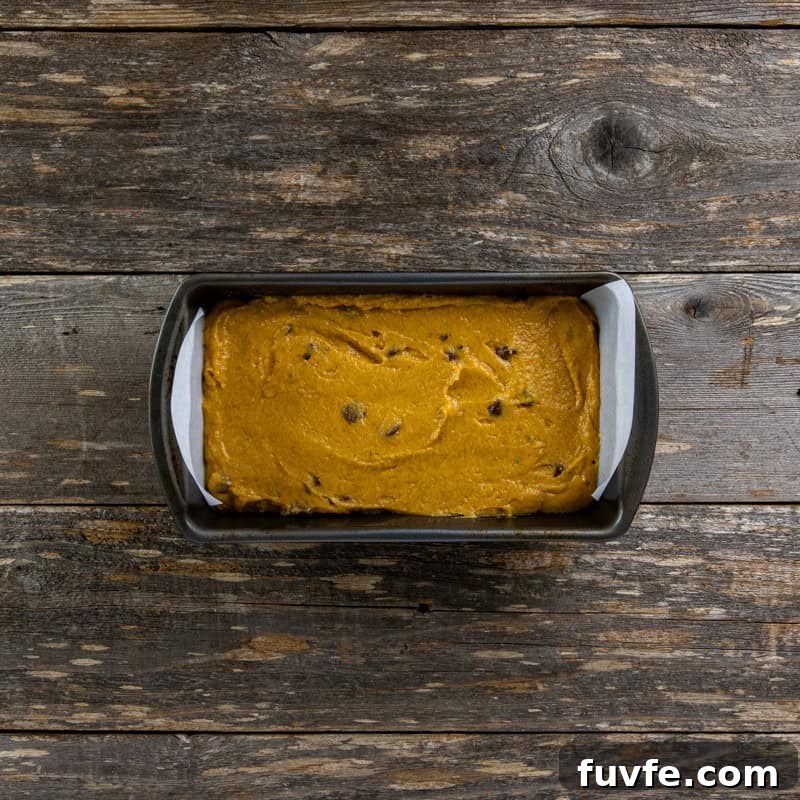 Batter poured into a 9 by 5-inch loaf pan with parchment paper handlews.