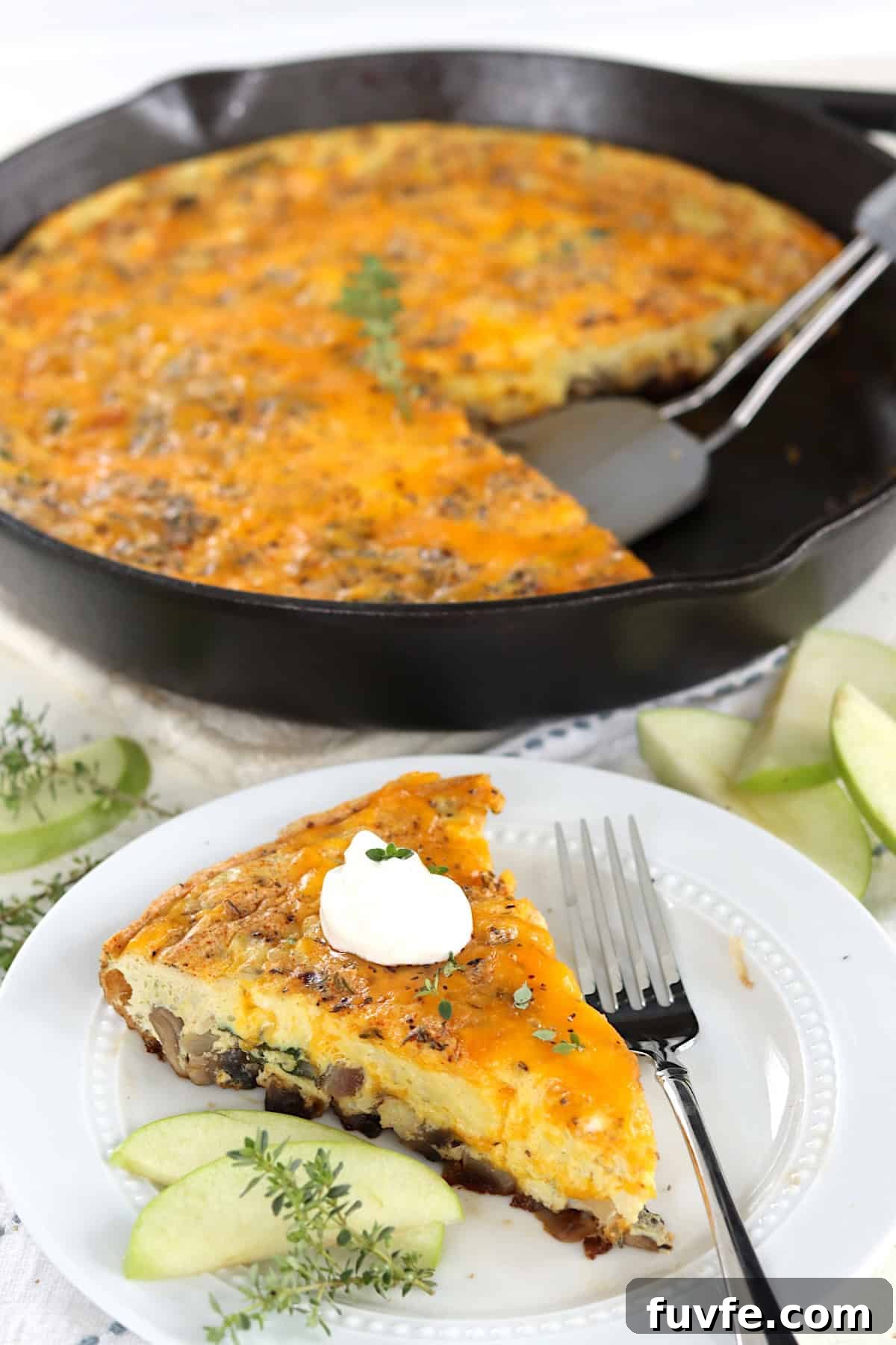 Apple Cheddar Frittata with Caramelized Onions and Herbs 8 A sliced of apple and cheddar egg frittata on a white plate with apple slices.
