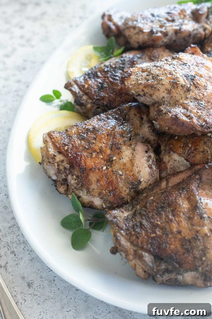 Grilled chicken thighs on a platter with lemon and oregano