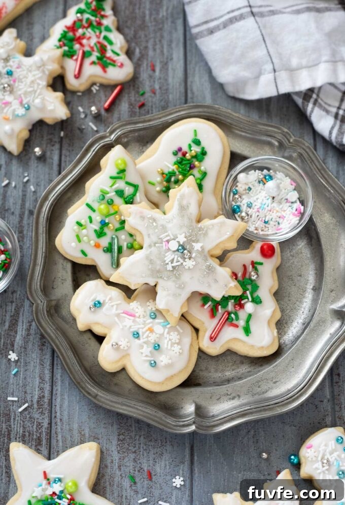 Christmas cut out cookies on a plate with a bowl of sprinkles.