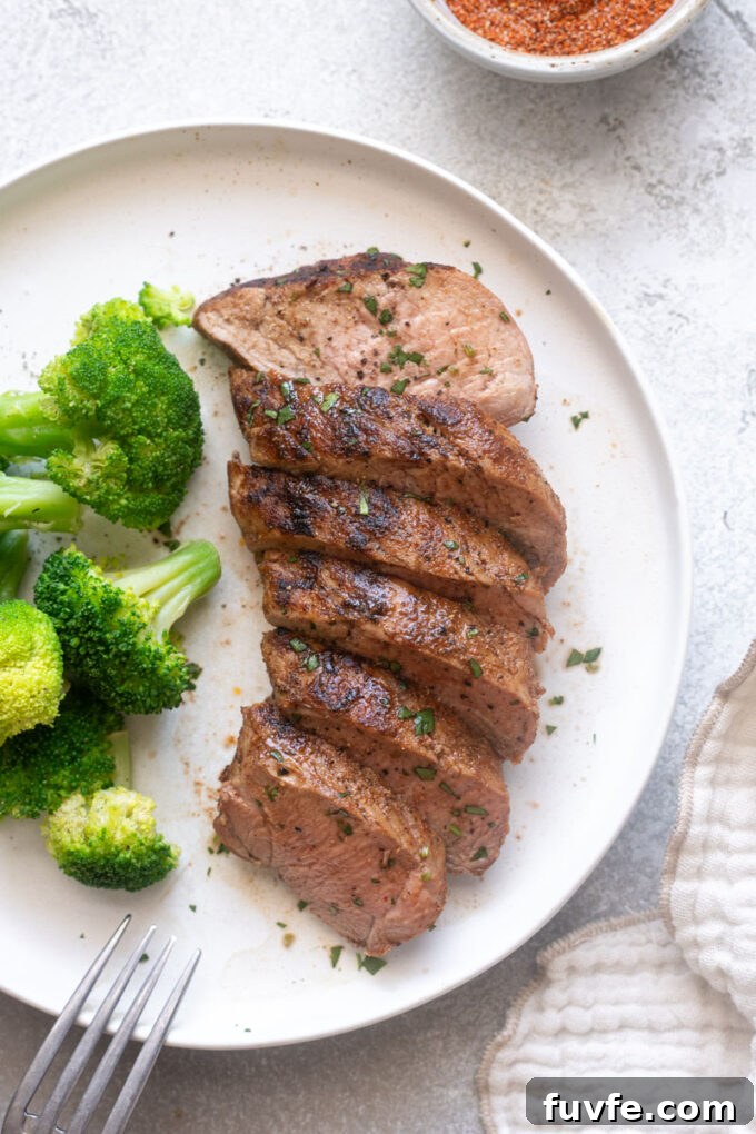 Juicy grilled pork tenderloin on a plate with broccoli.