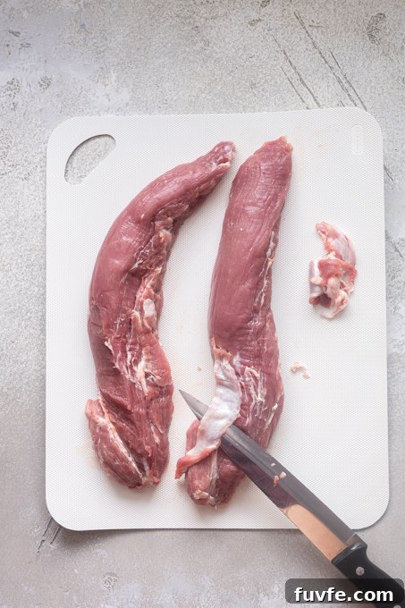 Knife cutting silver skin from pork tenderloin.
