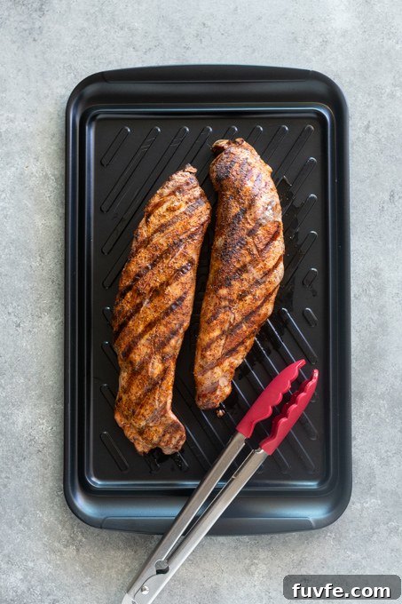 Grilled pork tenderloins resting on cutting board with tongs.