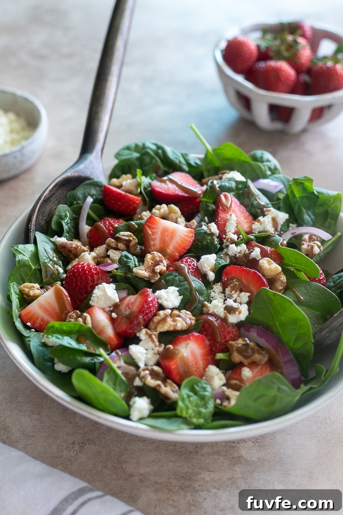 Spinach and strawberry salad in a white bowl with serving spoon