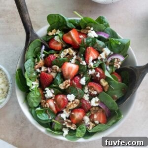 Strawberry spinach salad in a bowl with salad servers