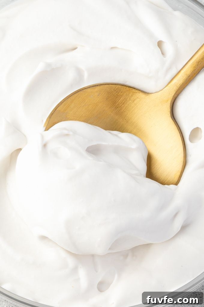 Coconut cream whipped cream in a bowl with spoon digging in.