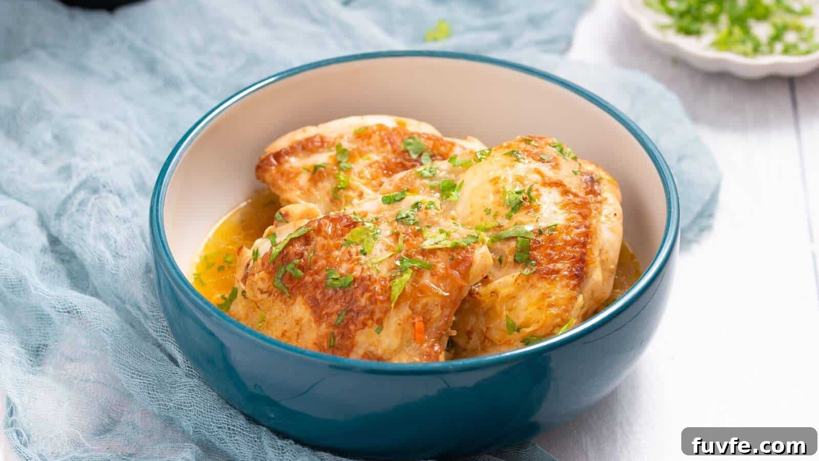 A blue bowl of cooked chicken breasts garnished with chopped herbs on a light fabric backdrop.