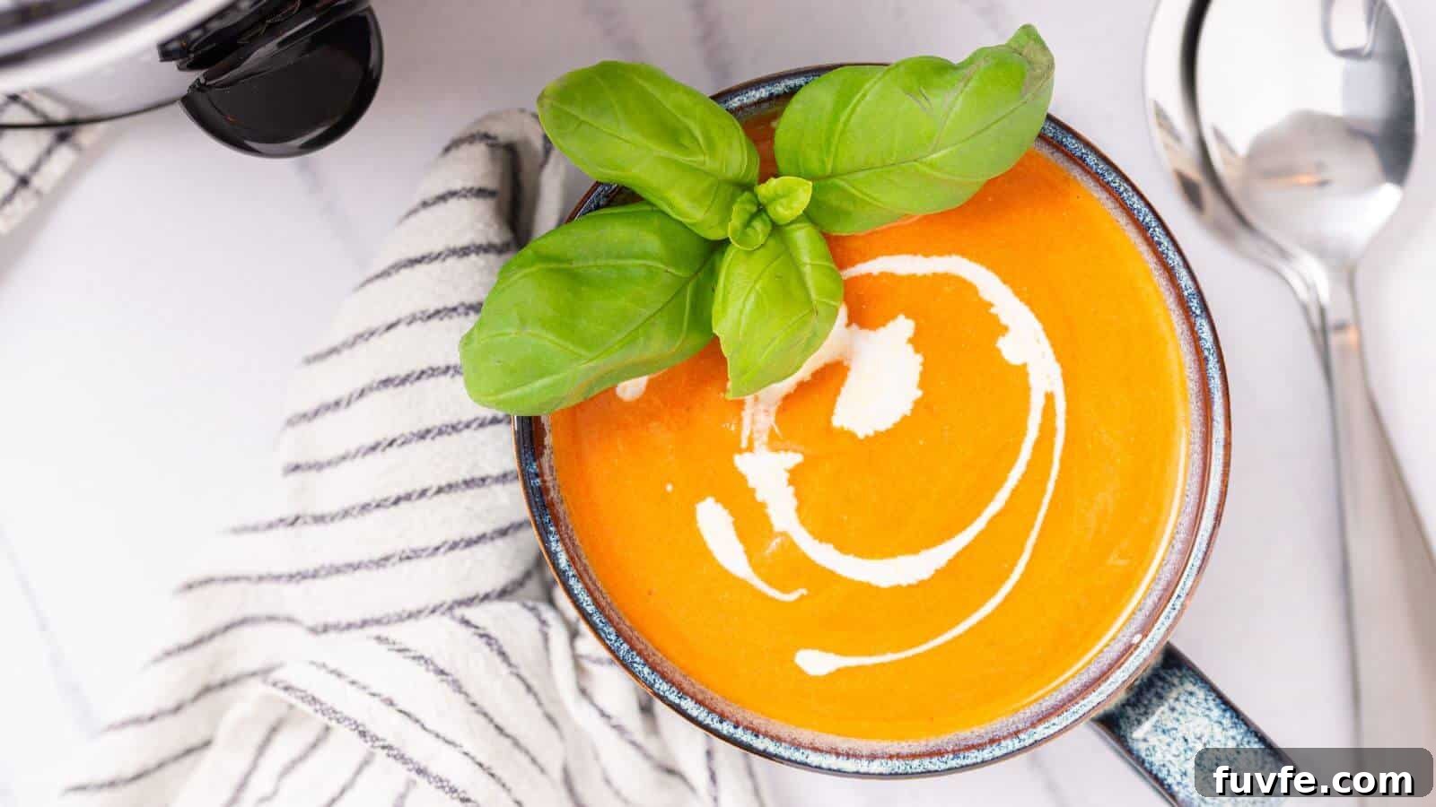 Top view of a bowl of creamy tomato soup garnished with basil, served with a spoon and sunglasses on the side.