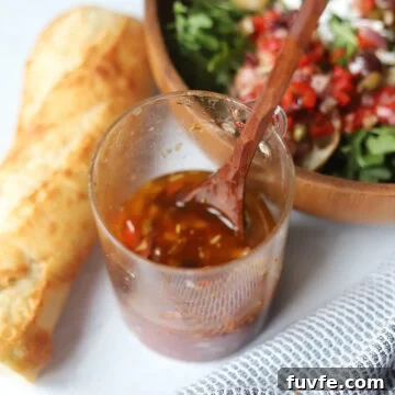 Puttanesca Vinaigrette: Bold Olive, Tomato & Anchovy Dressing 5 side view of homemade Puttanesca Vinaigrette next to a bowl of salad and a baguette.