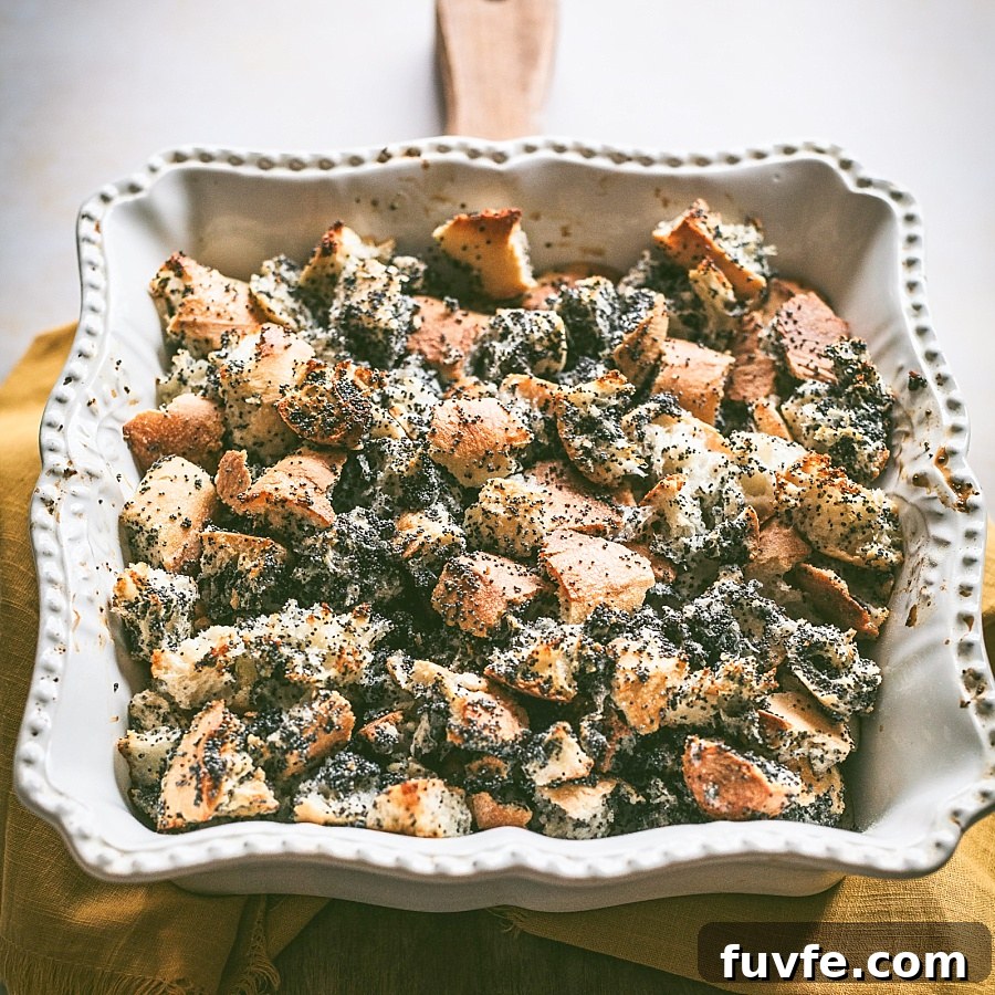 Gorgeously lit square casserole dish of simple Makos Goba, Hungarian Poppy Seed Bread pudding on rustic cutting board with mustard napkin