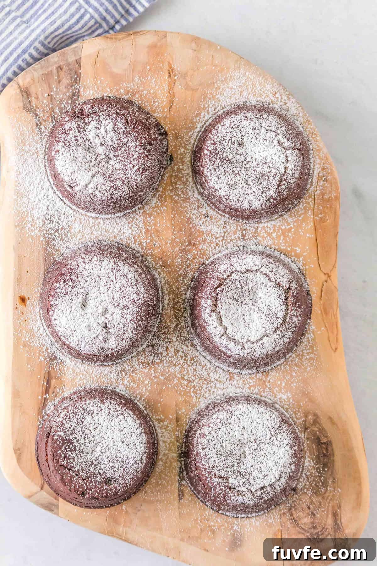 Decadent Chocolate Molten Lava Cake Recipe for Home Bakers 5 Six decadent Chocolate Lava Cakes dusted with powdered sugar, elegantly arranged on a wooden cutting board.