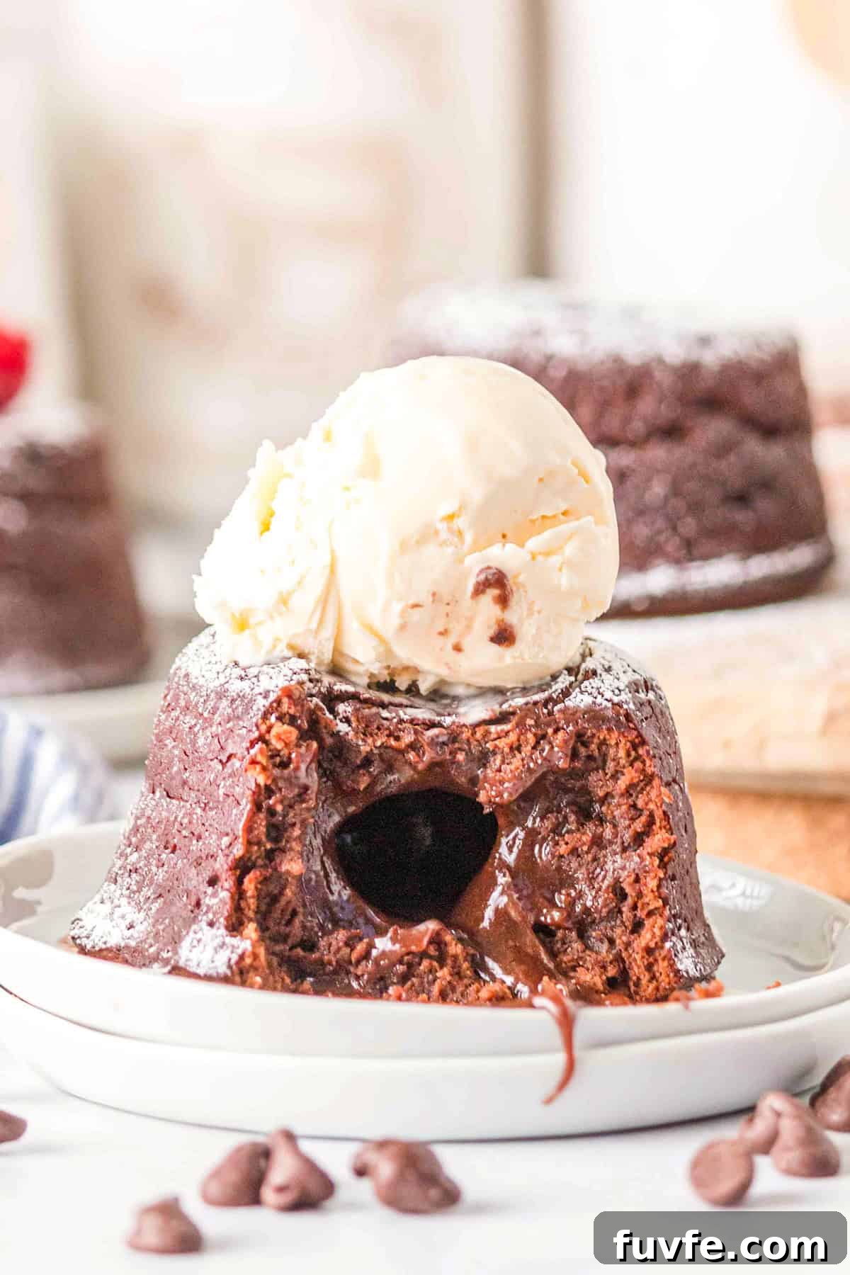 Decadent Chocolate Molten Lava Cake Recipe for Home Bakers 6 A decadent Chocolate Lava Cake with a molten center is topped with a scoop of vanilla ice cream on a white plate, surrounded by chocolate chips.