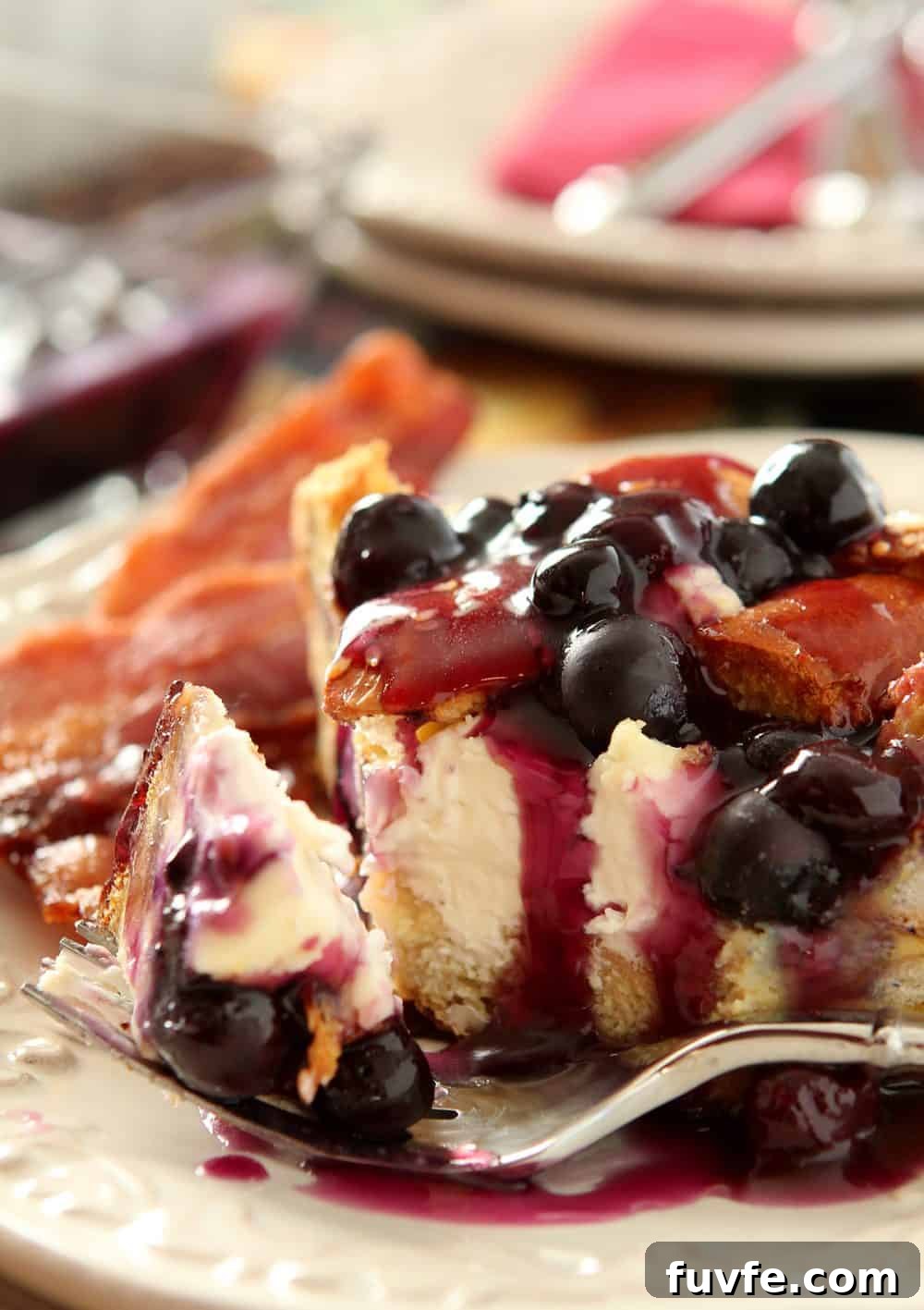 A slice of Blueberry and Cream Cheese Stuffed French Toast is on a plate with bacon strips.
