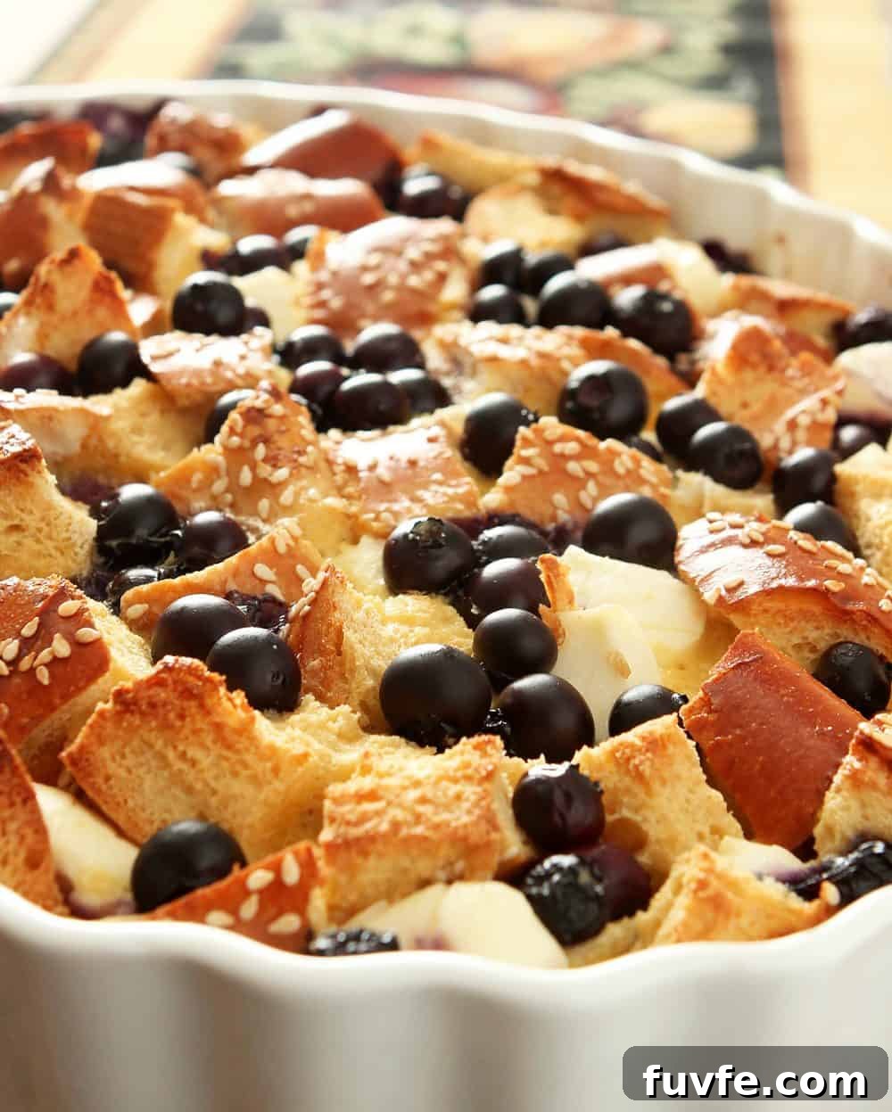 White Casserole dish filled with bread, eggs, cream cheese, and blueberries for a morning French toast baked treat.