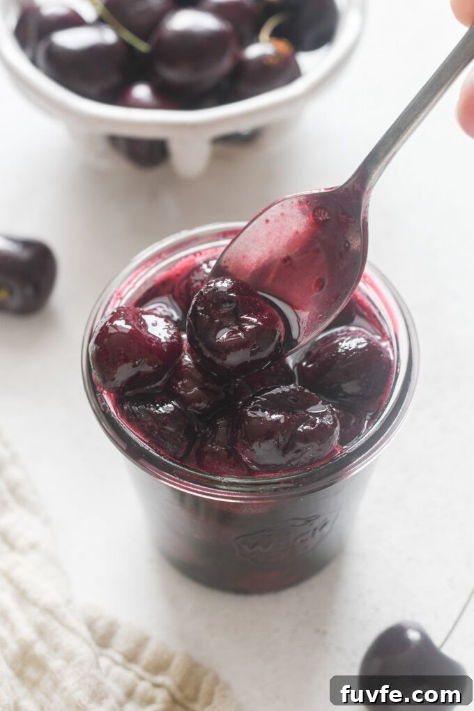 Homemade Cherry Compote Recipe for Desserts and Breakfast 2 Spoonful of cherry compote over a jar.