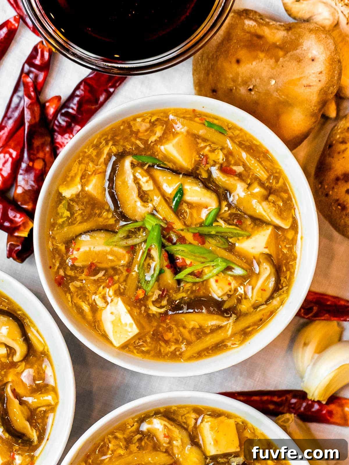 a bowl of Chinese hot and sour soup with mushrooms and tofu next to dried spicy chili peppers