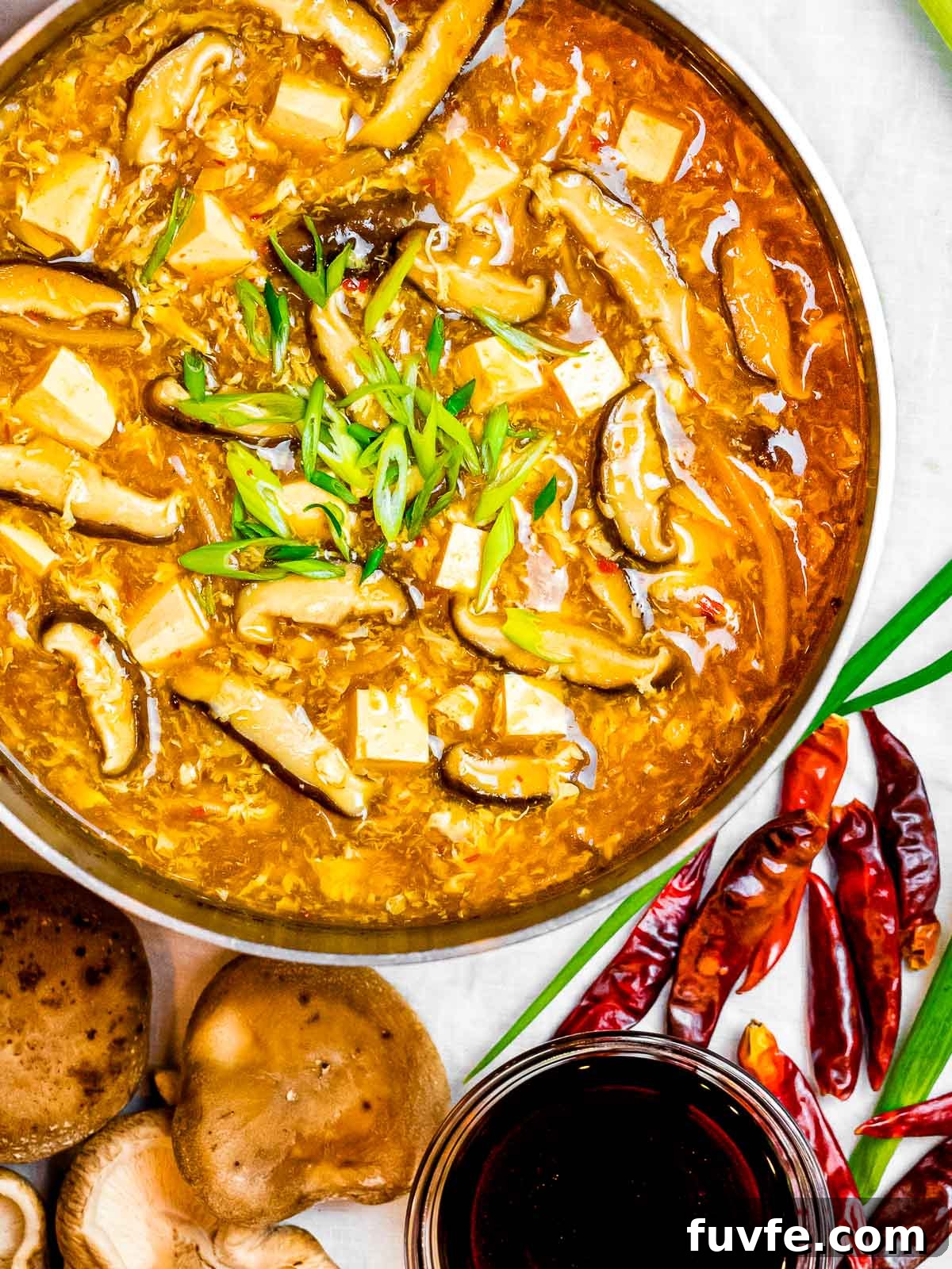 a pot of Chinese hot and sour soup surrounded with spicy chili peppers, shiitake mushrooms, and soy sauce