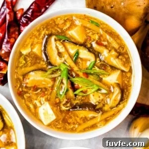 close up of Chinese hot and sour soup with mushrooms and tofu, next to dried hot chili peppers