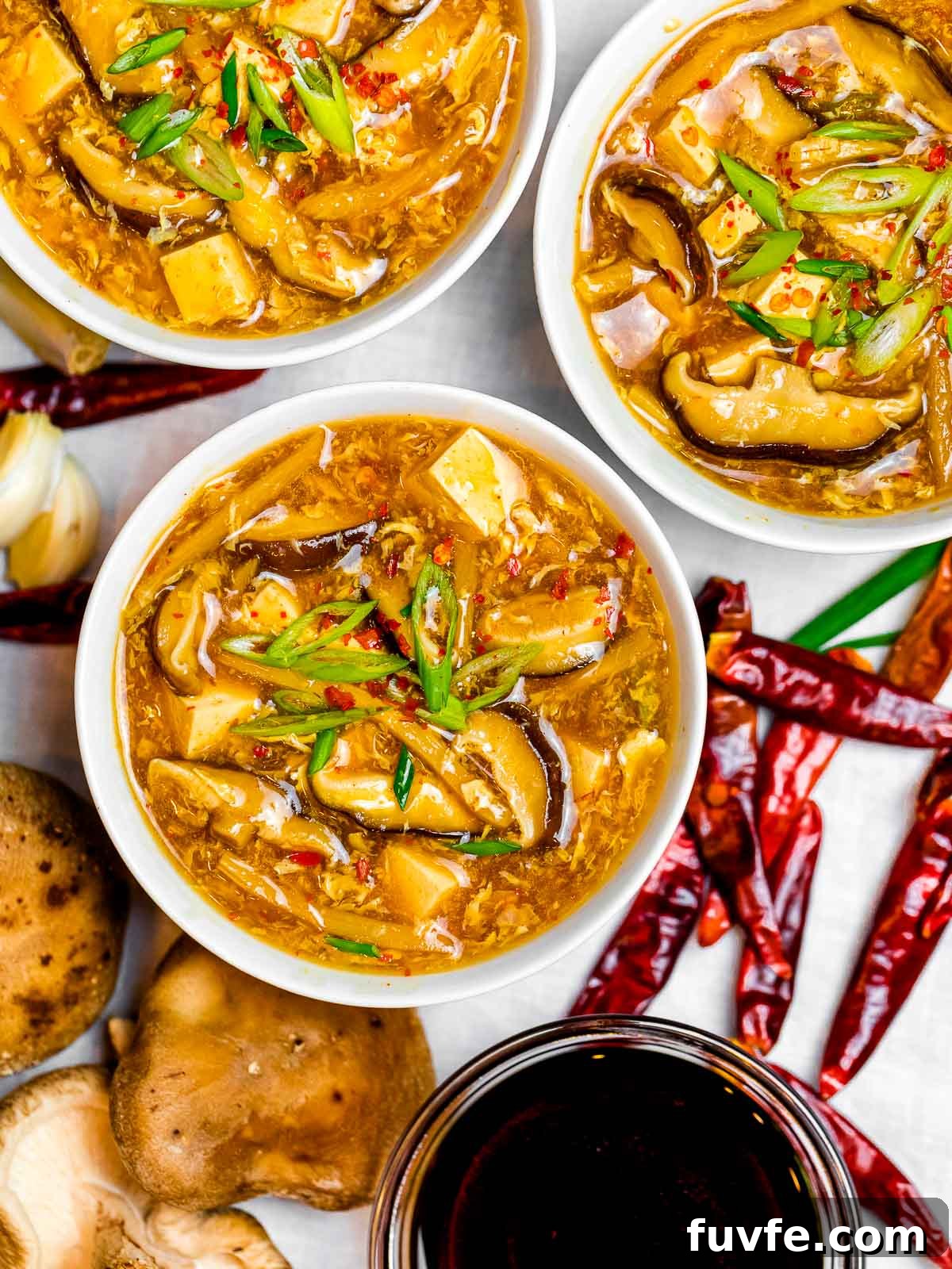 bowls of Chinese hot and sour soup with mushrooms, tofu, and scallions next to dried hot chili peppers