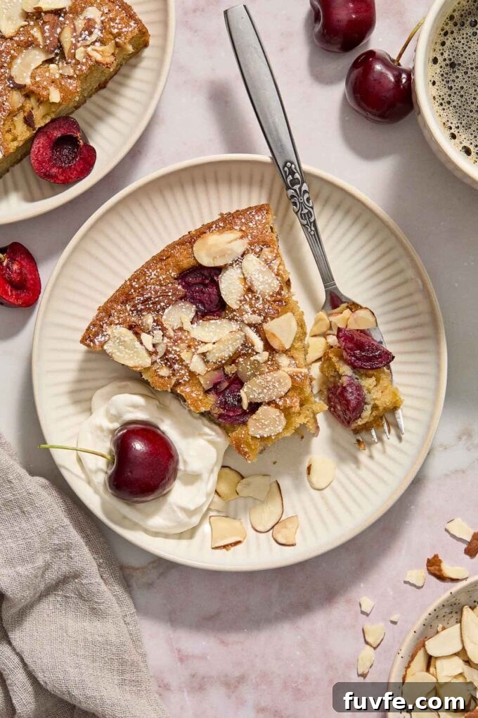 Slice of cherry and almond cake on a plate with whipped cream.