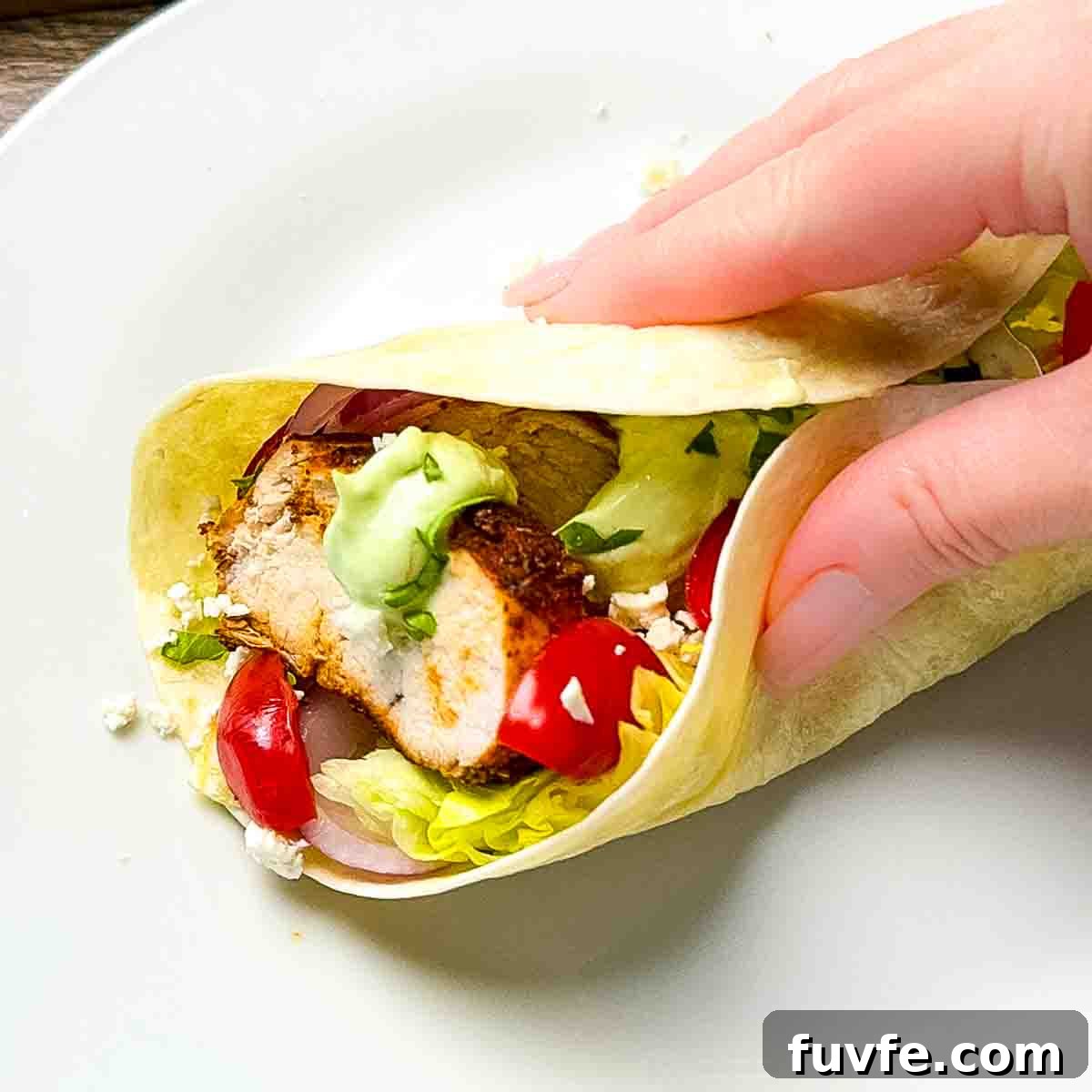 A blackened chicken taco rolled up on a plate and ready to eat.