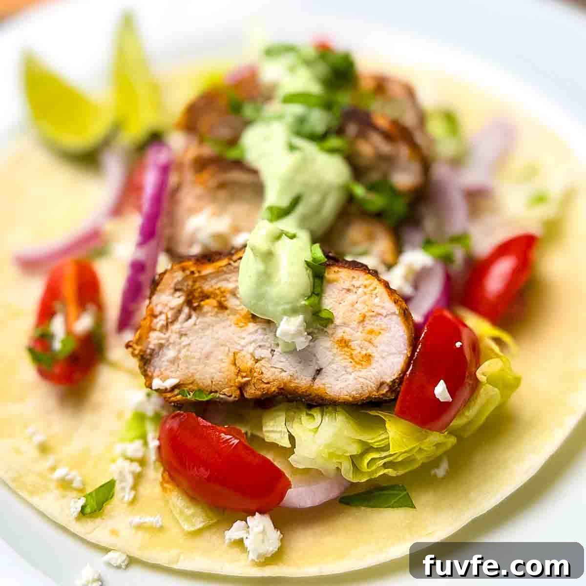 An assembled blackened chicken taco on a dinner plate with lime wedges.