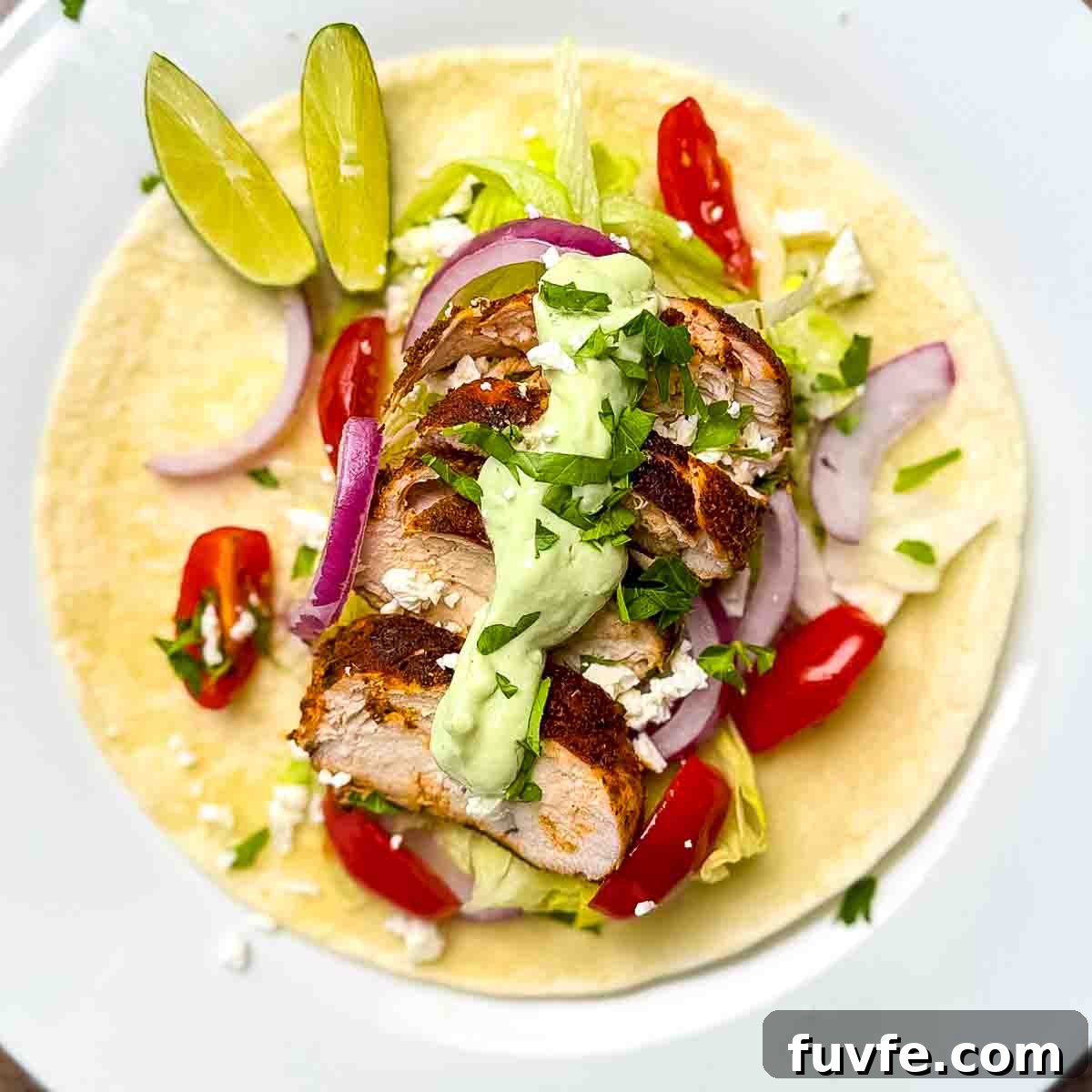 A plate of blackened chicken taco topped with avocado lime crema and cilantro.