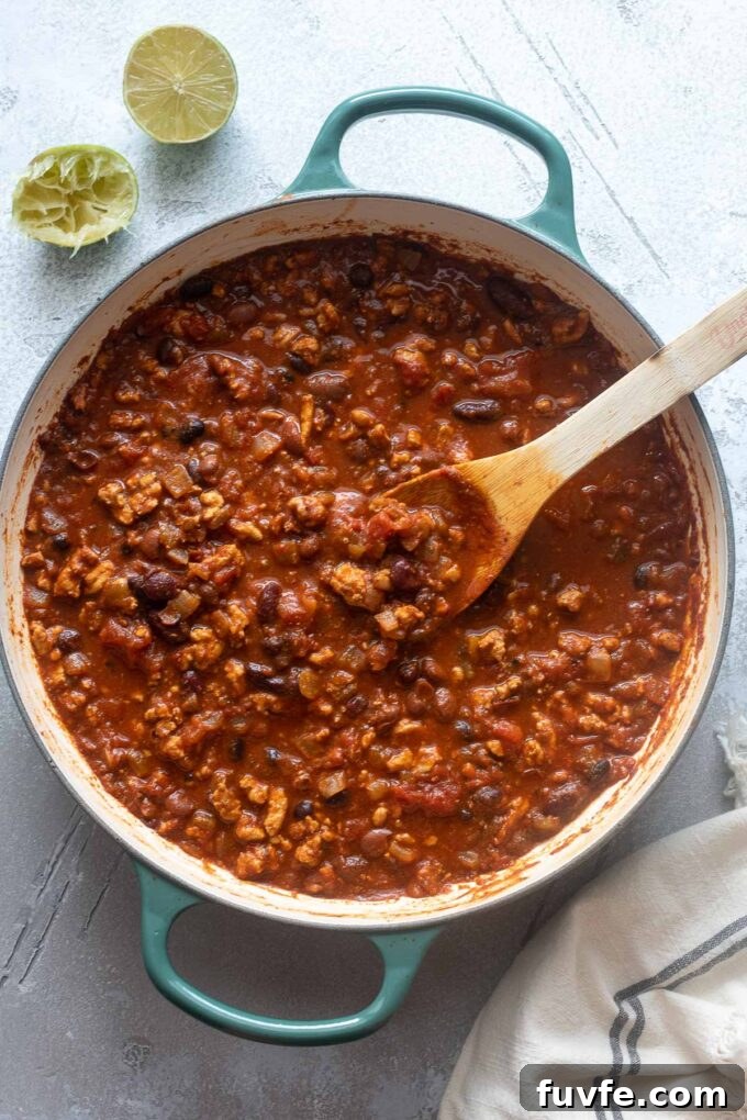 Ground chicken chili in a Dutch oven with wooden spoon digging in.