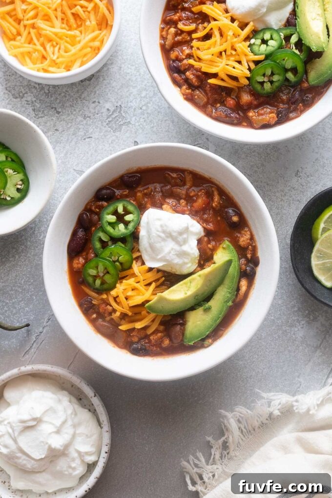 Ground chicken chili in a bowl surrounded by toppings.