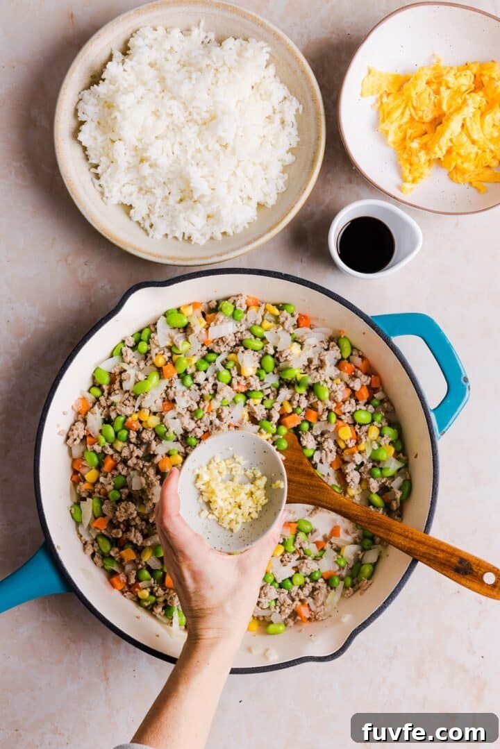 Savory Ground Turkey Fried Rice Recipe — Quick Weeknight Meal 9 Garlic being added to a pan with vegetables and ground turkey to prepare fried rice