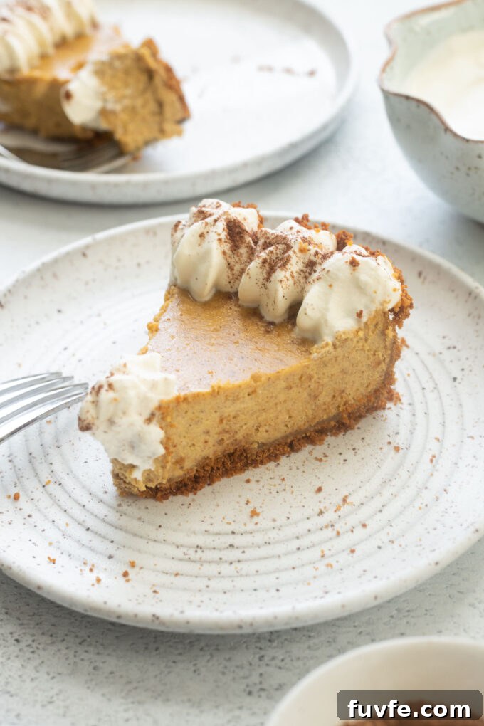 Slice of pumpkin cheesecake pie on a plate with piped whipped cream.