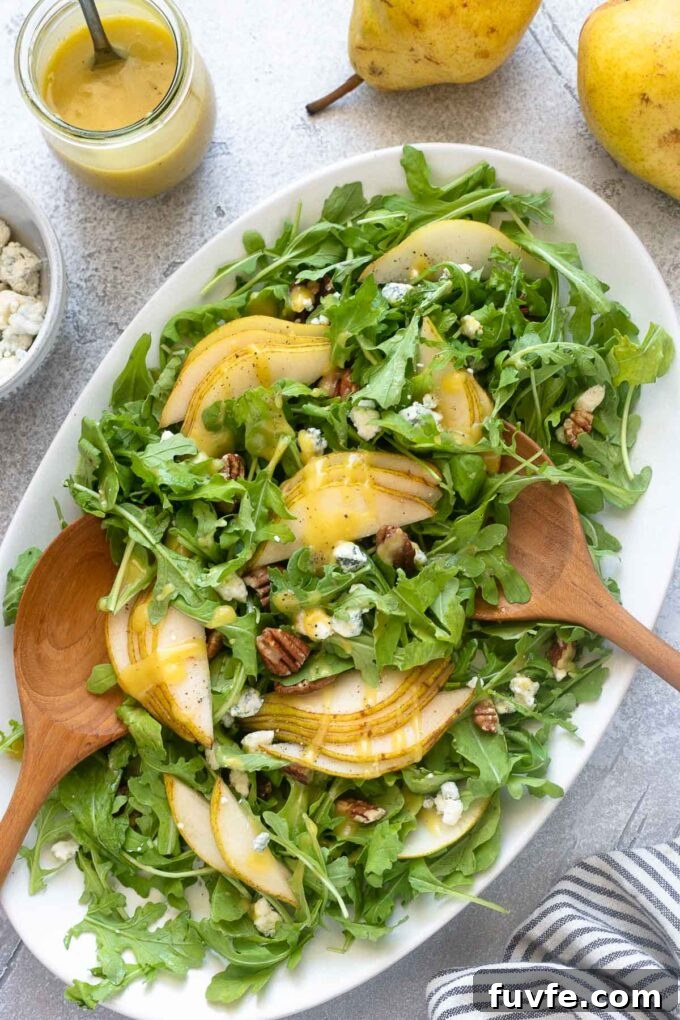 Arugula pear salad on a platter with wooden salad servers.