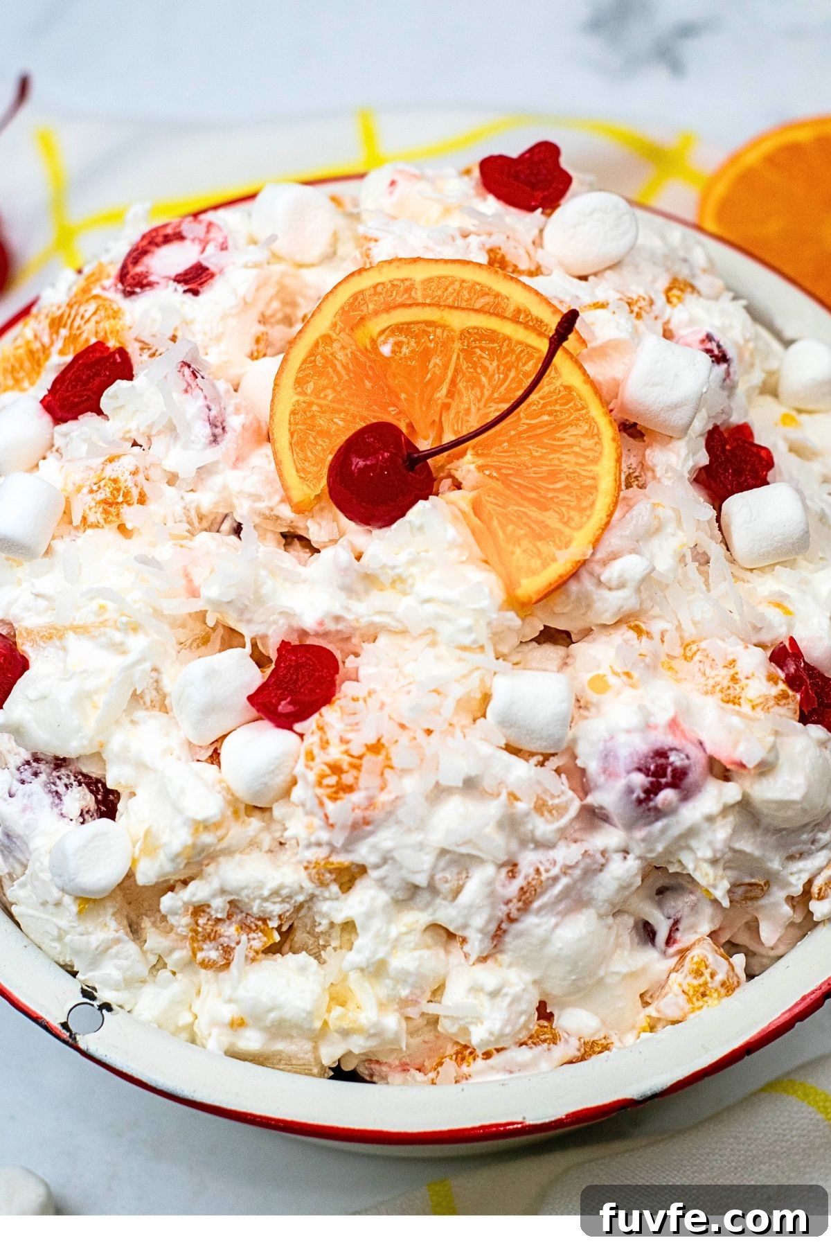 Large bowl filled with ambrosia salad, topped with orange slices and cherries. 