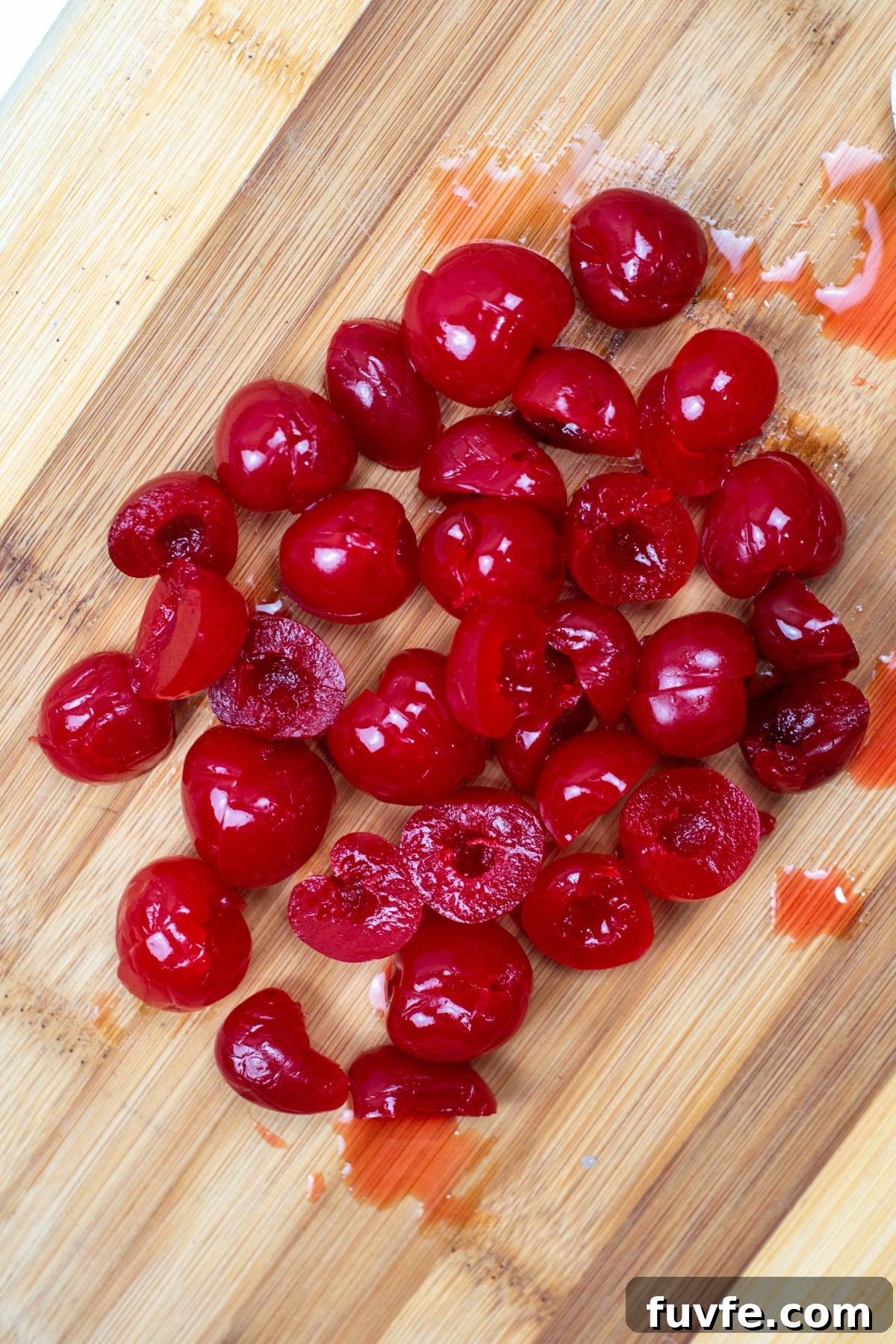 Maraschino cherries on a cutting board, being sliced in half. 