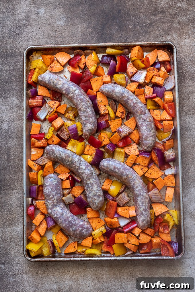 Italian sausage nestled into vegetables on baking sheet.