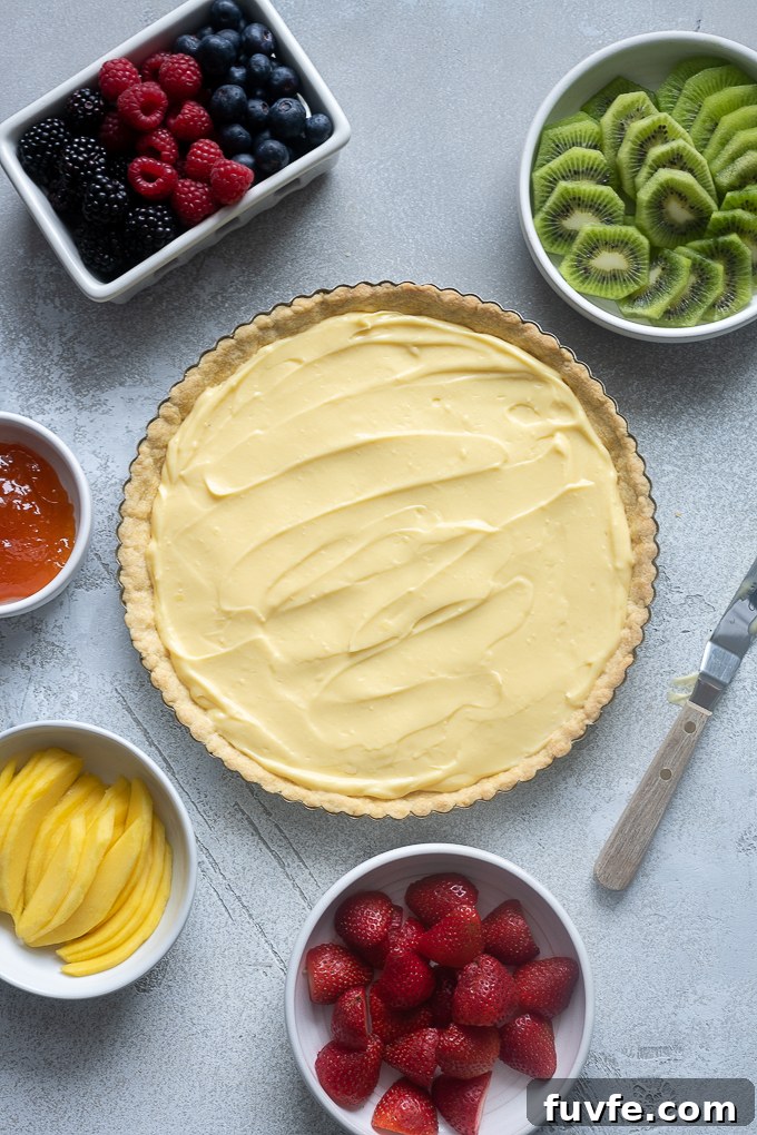 Tart crust filled with pastry cream and fresh fruit prepped in bowls.