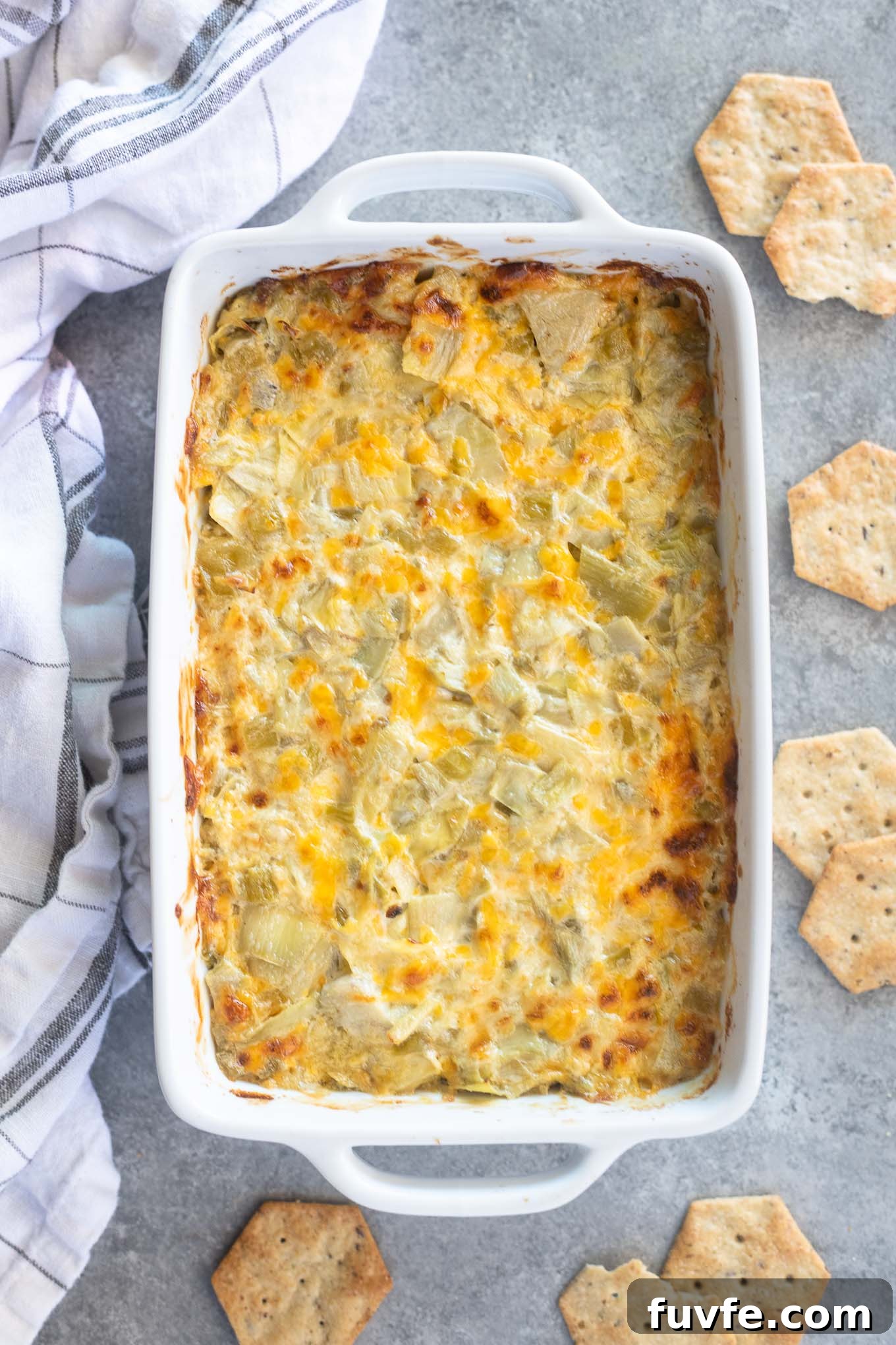 Hot artichoke dip in a baking dish with crackers