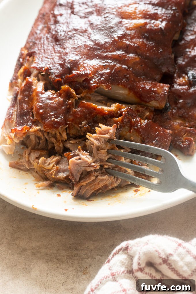 Fall-Off-the-Bone Slow-Cooker Baby Back Ribs 10 Slow cooked BBQ baby back ribs on a platter with fork pulling them apart.