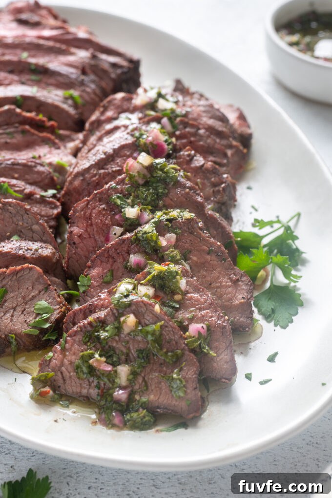 Grilled tri tip roast sliced on a platter with chimichurri sauce.