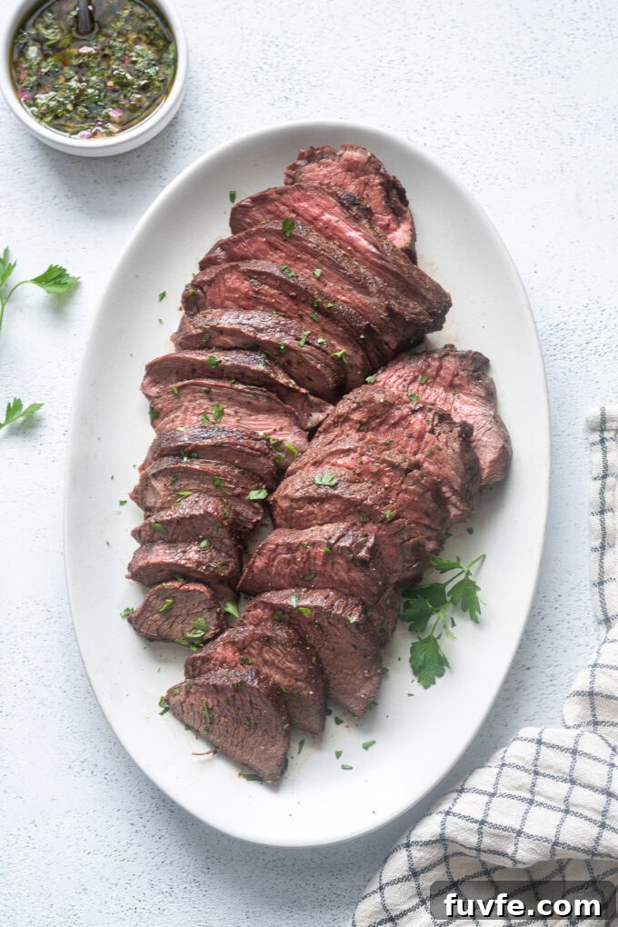 Sliced grilled beef tri tip roast on a platter with chopped parsley.