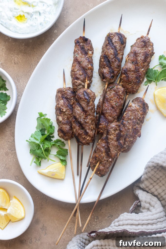 Lamb kofta kebabs on a serving platter with herbs and lemon.