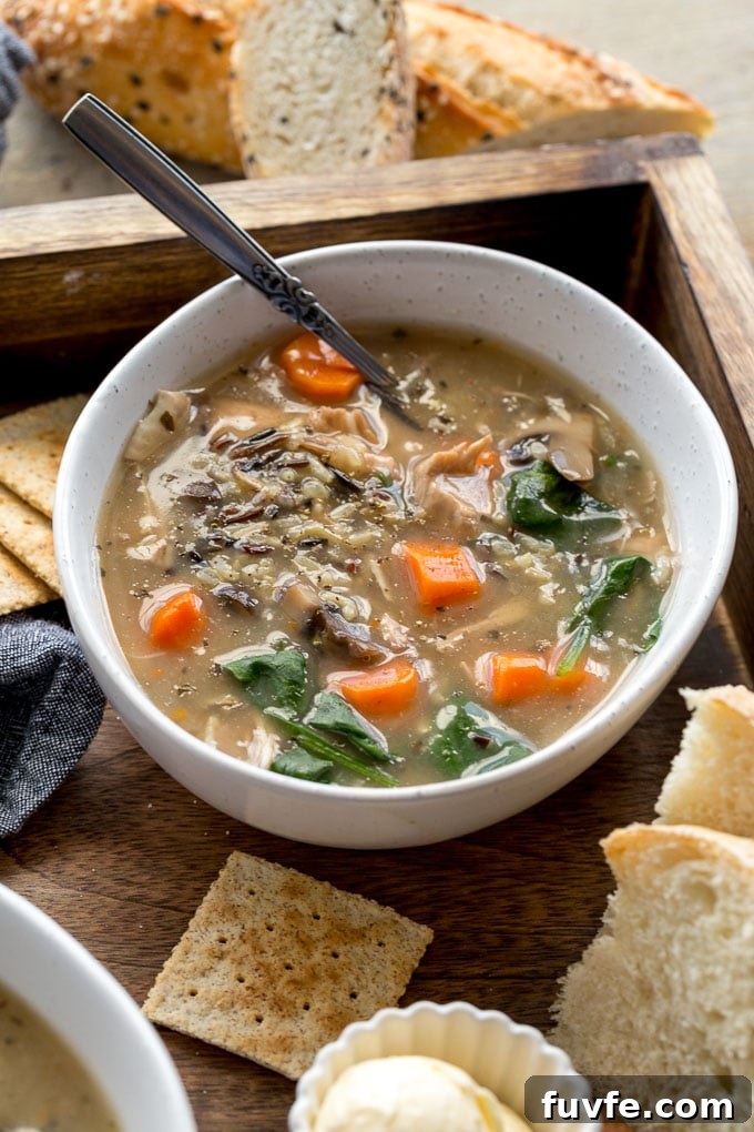 Chicken and wild rice soup in a white bowl and placed in a wooden tray with crackers and bread.